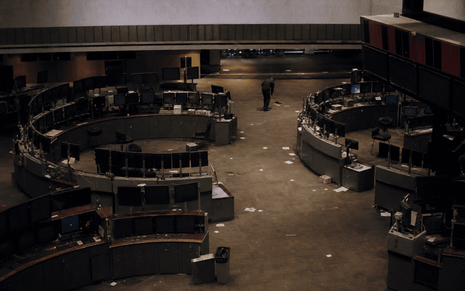 A maintenance worker sweeps papers from the floor of a stock exchange after closing