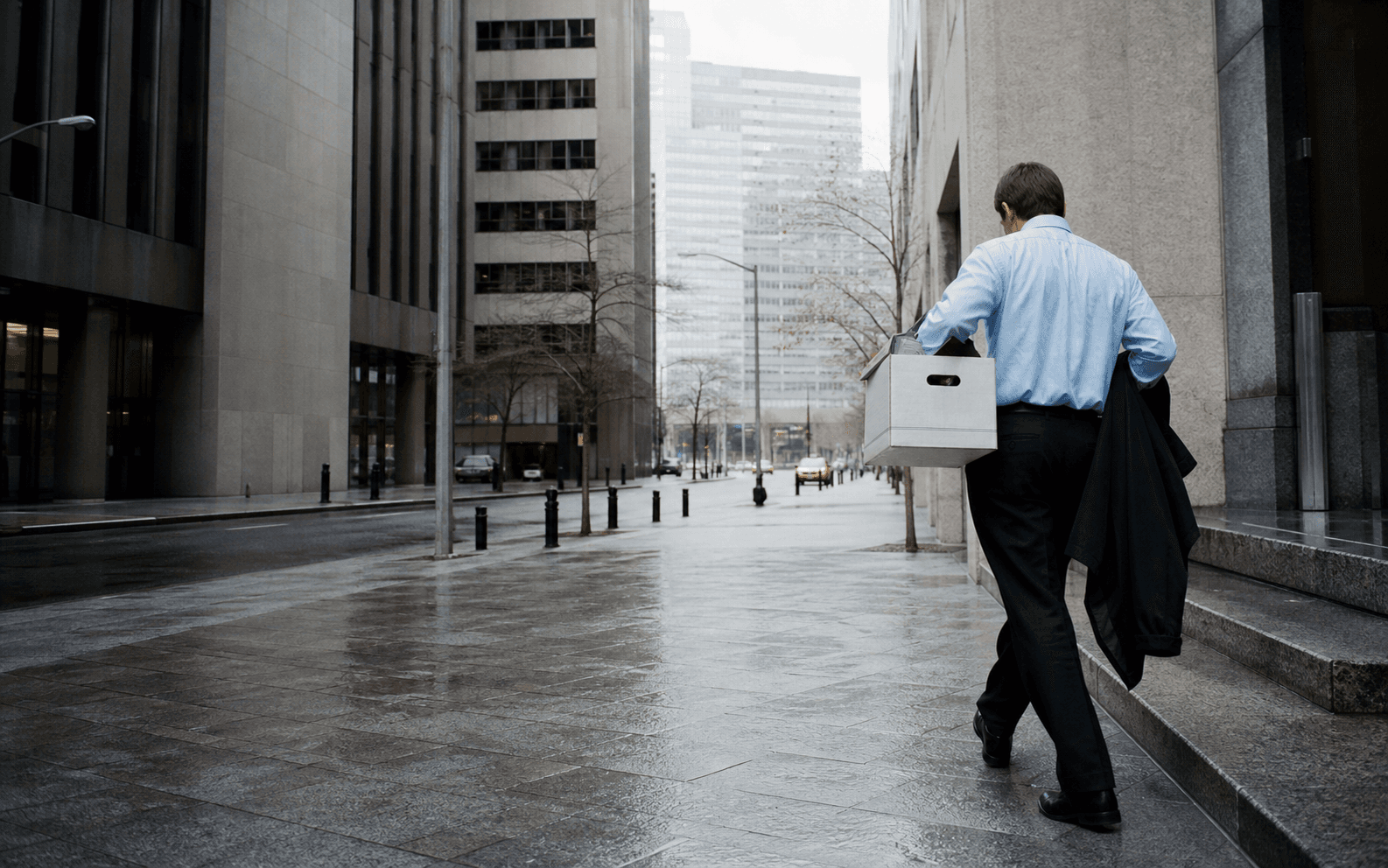 A finance worker carries a box away from an office building on a grey day in Manhattan
