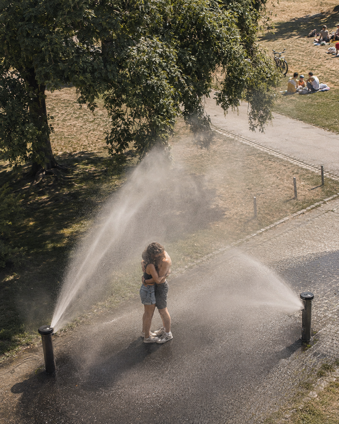 Scena concettuale: una coppia si abbraccia sotto gli spruzzi degli irrigatori in un parco.